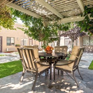 A cozy patio setup with a table and chairs under a pergola surrounded by greenery.