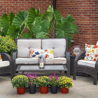 A cozy outdoor patio setup with a sofa, chairs, colorful cushions, and potted plants against a brick wall.