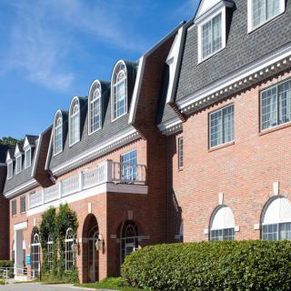 A row of brick buildings with arched windows and a sloped roof under a clear blue sky.