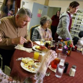 A group of elderly individuals enjoying a meal together at a community dining table.