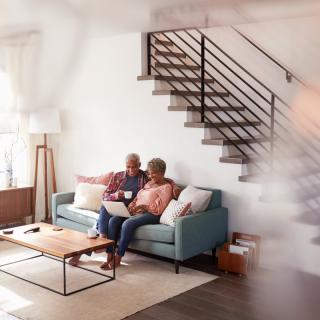 A couple relaxes on the sofa in their living room, engaging with a laptop and enjoying each other's company.