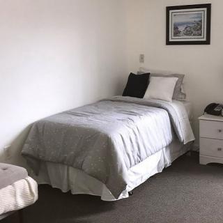 A minimalist bedroom featuring a single bed with gray bedding and a nightstand.