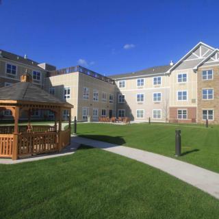 A residential apartment complex with a well-maintained lawn and a gazebo under a clear blue sky.