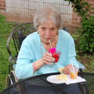 An elderly woman enjoying a drink and snacks while sitting outside in a garden.
