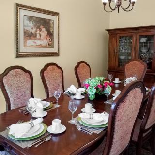 A dining room with a neatly set table, surrounded by upholstered chairs and adorned with a floral centerpiece.
