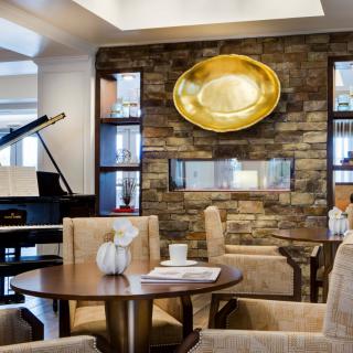A modern lounge area featuring a grand piano, plush seating, and a stone fireplace adorned with an abstract art piece.