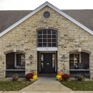 A stone building entrance decorated with fall flowers and pumpkins.