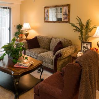 A cozy living room with a sofa, armchair, and coffee table, accented by plants and warm lighting.