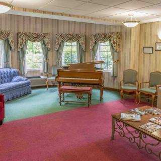 A cozy living room with a piano, seating area, and large windows.
