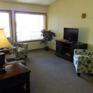 A cozy living room with a television, patterned chairs, and large windows.