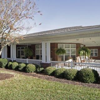 A well-maintained building with a porch, surrounded by neatly trimmed bushes and greenery.