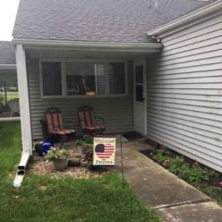 A small porch with two chairs and a sign in front of a house.