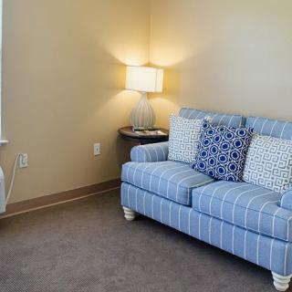 A cozy living room corner featuring a striped couch with decorative pillows and a lit lamp on the side table.