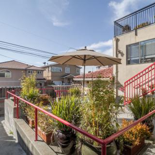 An outdoor patio with potted plants and an umbrella, adjacent to a building in an urban setting.