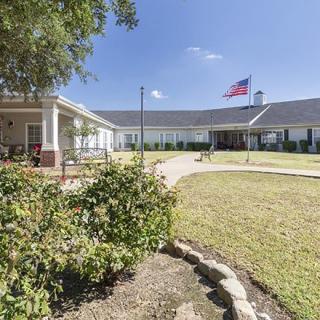 A large building with a garden and a pathway leading to the entrance, featuring an American flag flying in the yard.