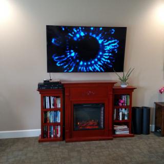 A cozy living room setup features a wall-mounted television above a fireplace with books and decor on the shelves.
