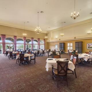 An elegant restaurant dining room with neatly arranged tables and chairs, illuminated by chandeliers.