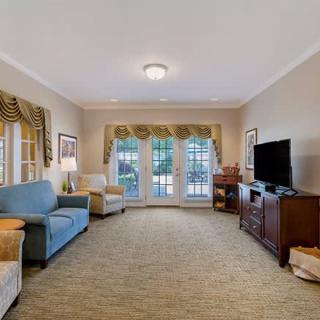A spacious living room featuring comfortable seating, a television, and large windows with elegant curtains.