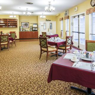 A spacious dining room with neatly arranged tables and chairs, set against a carpeted floor and large windows.