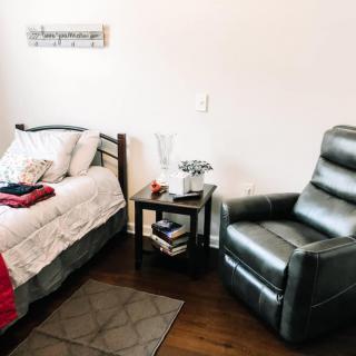 A cozy bedroom featuring a neatly made bed, a comfortable armchair, and a side table with books.