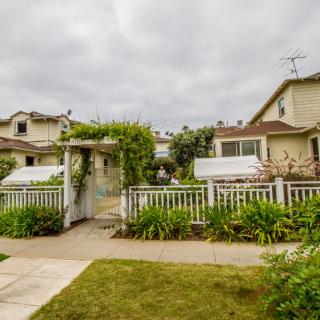 A charming house with a fenced garden and a pathway under a cloudy sky.