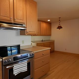 A modern kitchen with wooden cabinets, a stainless steel stove, and wood flooring.