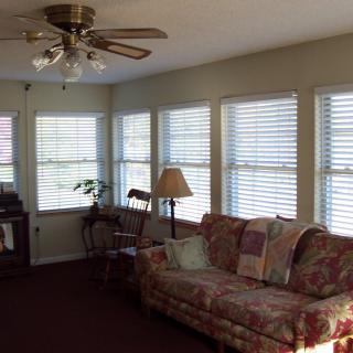 A cozy living room with a floral sofa, multiple windows with blinds, and a ceiling fan.