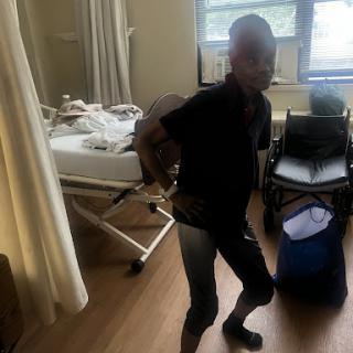 A person in a hospital room, standing near a bed and some medical equipment.