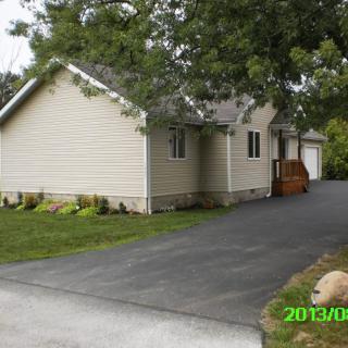 A suburban house with a paved driveway surrounded by trees and a well-kept lawn.