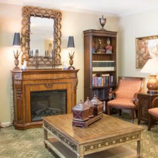 A cozy living room with traditional decor, featuring a fireplace, ornate mirror, bookshelf, and comfortable armchairs.
