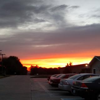 A beautiful sunset paints the sky with vibrant colors, viewed from a quiet parking lot.