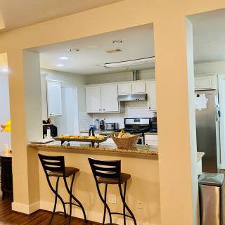 A modern kitchen with a bar counter and two stools, showcasing sleek appliances and home decor.