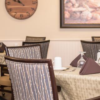 A cozy dining area with neatly arranged tables and chairs, featuring a wall clock and artwork.