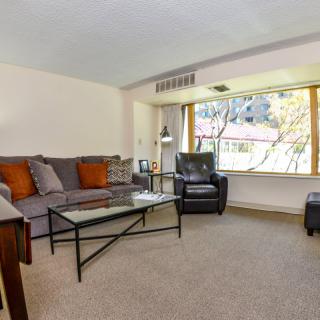 A cozy living room featuring a sofa, armchair, and coffee table with a large window providing natural light.