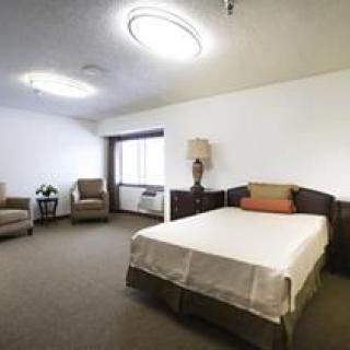 A minimalist hotel room with a bed, chairs, and a side table.