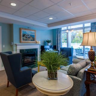 A cozy living room with comfortable seating and a fireplace, featuring a decorative plant and ample natural light from the windows.