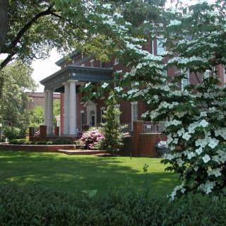 A beautiful brick house surrounded by a lush garden with blooming trees and flowers.
