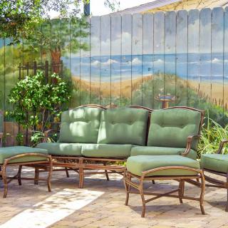 A cozy outdoor patio setting with green cushioned furniture and a beach-themed mural on a wooden fence.