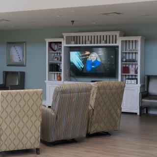 A cozy seating area with patterned chairs facing a television, surrounded by shelves.