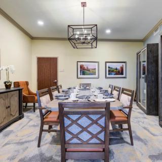 A well-appointed dining room features a large table set for a meal, surrounded by wooden chairs and illuminated by a modern chandelier. Decor includes framed artwork on the walls.