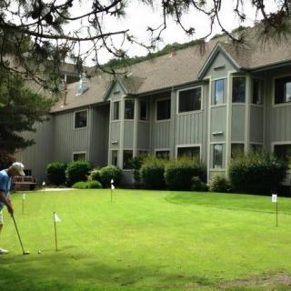 A person practicing golf on a putting green near a residential building.