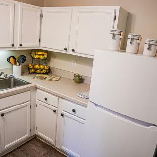 A cozy kitchen featuring white cabinets, a refrigerator, and countertop accessories including a fruit basket and jar containers.