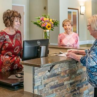 A receptionist and visitors interacting at a front desk in an office setting.