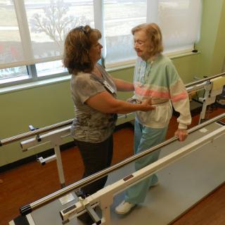 A healthcare professional assists an elderly patient during a physical therapy session.