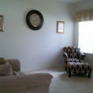 A cozy living room with a sofa, patterned chair, wall clock, and window.