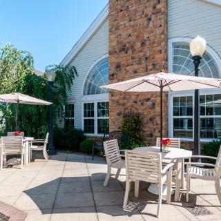 A sunny outdoor patio area with tables, chairs, and umbrellas adjacent to a building.