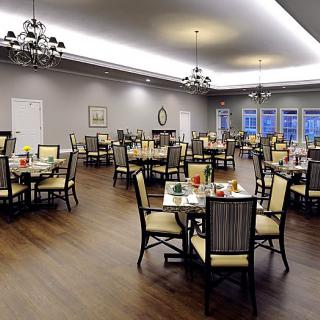 An elegant dining room with neatly arranged tables and chairs, lit by chandeliers.