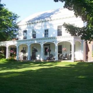 A white house with a large porch and a well-maintained lawn surrounded by trees.