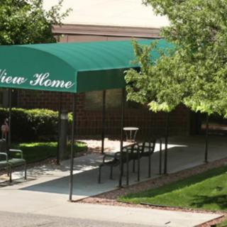 A building entrance with a green awning labeled 'Home' surrounded by trees and shrubs.