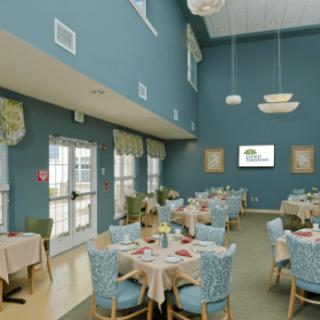 A spacious dining room with blue walls, set with tables and chairs, featuring elegant lighting fixtures.